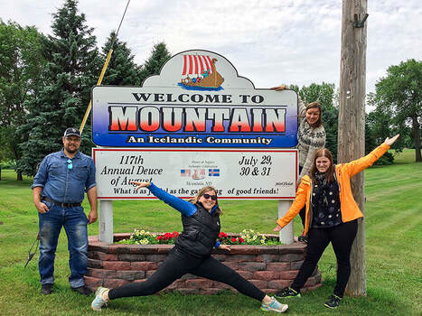 four past participants posing with the sign for Mountain, North Dakota