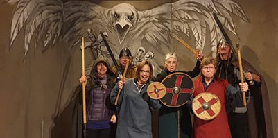 2019 Snorri Plus participants dressed as vikings while visiting the Saga Museum in Reykjavík, Iceland. The mural on the wall behind them features a large raven in flight.